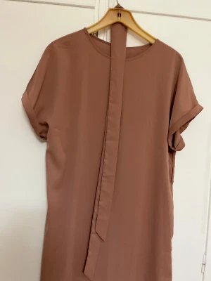 Beige kort klänning från SHEIN XL - Enkel och stilren beige kort klänning från SHEIN i storlek XL. Klänningen har rund halsringning, korta ärmar med uppvik och ett dekorativt band framtill. Tillverkad i ett mjukt, lätt syntetmaterial som ger en skön känsla.