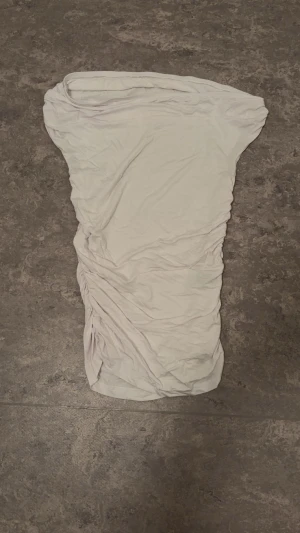 Vit one shoulder top med rynk - Säljer en vit bandeau tubtopp med snygga rynkade detaljer på ena sidan. Toppen är axelbandslös och har en tight passform som framhäver siluetten. Perfekt för dig som gillar minimalistisk stil och vill ha en enkel men trendig topp.