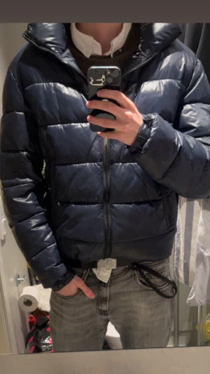 Jacka  BOSS - Säljer en mörkblå dunjacka från BOSS med glansig finish. Jackan har huva, två dragkedjefickor och quiltad design. Perfekt för kalla dagar,ny pris ca 2000kr