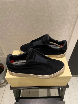 Axel Arigato 360 svartvita  - Svartavita slip-on Axel Arigato sneakers med mörkblå mockaöverdel med vit sula. Skorna har använts ett par gånger, men har slutat använda dessa nu för det är ej min stil länger. 