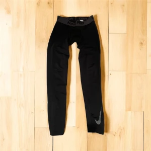 Nike Pro svarta träningsleggings M - Nike Pro svarta leggings med Dri-Fit-teknologi, perfekt för träning. De har en elastisk midja med Nike Pro-logga och en diskret Swoosh på benet. Materialet är syntetiskt och designen är tight för maximal rörelsefrihet.