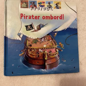 Pirater ombord! - Upptäck piraternas värld med denna interaktiva faktabok! Snurra, lyft och dra för att avslöja hemligheter om livet ombord på ett piratskepp. Perfekt för unga äventyrare som vill veta mer om piraternas spännande liv och deras fartyg.