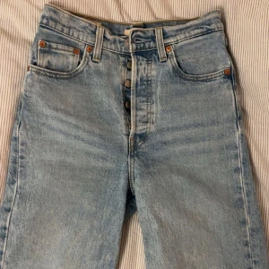 Levi's Ribcage Straight ljusblå jeans - Säljer ett par Levi's Ribcage Straight jeans i ljusblå tvätt med klassisk femficksdesign och knappgylf. Jeansen har hög midja och raka ben, tillverkade i slitstarkt denim med snygga detaljer som bruna sömmar och Levi's patch bak.