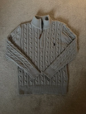Grå stickad half zip tröja Polo Ralph Lauren - Säljer en grå stickad tröja från Polo Ralph Lauren med half zip och klassiskt kabelstickat mönster. Tröjan har långärmade ribbade muddar och hög krage. Ikoniska Polo-loggan broderad på bröstet. Perfekt för dig som gillar stilren och tidlös design. Storleken är L men passar mer som S/M 🇨🇳