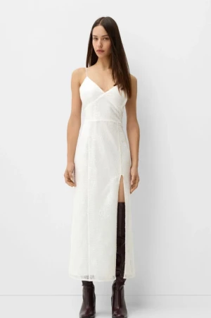 Vit glittrig långklänning med slits - Supersnygg vit långklänning med tunna axelband, v-ringning och glittrig yta. Klänningen har en smickrande omlott-look upptill och en hög slits på ena sidan. Perfekt för dig som vill sticka ut med en elegant och trendig look.