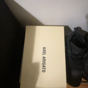 Grå sneakers Axel Arigato med dragkedja - Snygga grå sneakers från Axel Arigato i skinn med vit sula och dragkedja framtill istället för klassisk snörning. Minimalistisk design med rund tå och låg profil, perfekt för en clean och modern look.