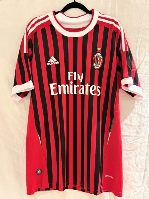 AC Milan fotbollströja Ibrahimović #11 - Säljer en AC Milan fotbollströja  med Ibrahimović och nummer 11 på ryggen. Tröjan har klassiska röda och svarta ränder, vit krage och vita detaljer vid ärmarna. Materialet är lätt polyester med klubbmärke på bröstet.