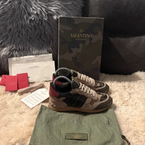 Valentino Rockrunner sneakers camouflage - Säljer ett par Valentino Rockrunner sneakers med snyggt kamouflagemönster i grönt, beige och svart. Skorna har detaljer i mocka och skinn, samt ikoniska nitar vid hälen. Platt sula och rund tå, med snörning framtill. Kommer med originalkartong, dustbag, kvitto, flera valentino kort och extra skosnören. Tveka inte att fråga om du har någon fråga🙂