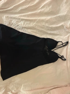 Svart sexig pyjamas spetsklänning - Säljer en svart kortklänning med tunna axelband och vacker spets upptill. Klänningen har en slät kjol i mjukt material och detaljer med spets kupa över bysten.  En svart sexig pyjamas spetskläning 