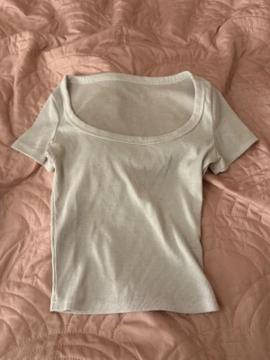 Vit ribbad topp med kort ärm - Säljer en vit ribbad topp med korta ärmar och bred, rundad halsringning. Toppen är slim i passformen och har en enkel, stilren design som funkar till många olika looks. Perfekt för dig som gillar basic plagg med lite extra detalj i strukturen.