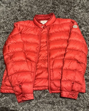 moncler acorus röd (ÄKTA) - Här är vår 10/10 moncler acorus jacka i röd. Perfekt för kyligare nätter och sticker utt med stil. Jackan är i storlek 3/M och har 2 fickor dragkedja och knappar vid armarna mvh Amore 