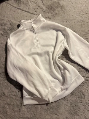Oversized mysig tröja  - Säljer en stilren vit sweatshirt med half zip och hög krage. Tröjan har långärmade ärmar och ribbade muddar vid ärmslut och nederkant. Perfekt för dig som gillar enkel och clean stil. Materialet känns mjukt och bekvämt. Helt ny!!
