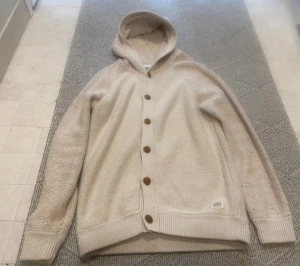 Beige stickad hoodie från Jack & Jones - Säljer en beige stickad hoodie från Jack & Jones Originals. Tröjan har långa ärmar, knappar framtill och en skön huva. Materialet är mjukt och har små färgprickar som ger en cool touch. Perfekt för dig som gillar avslappnad stil.
