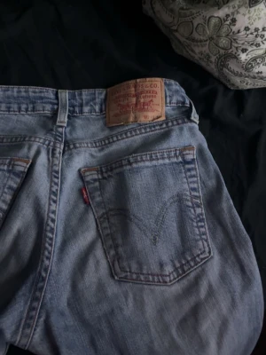 Levi's 517 ljusblå jeans bootcut - Ljusblå Levi's 517 jeans med klassisk bootcut och fem fickor. Snygga slitningar framtill och ikonisk läderpatch bak i midjan. Jeansen har normal passform och är tillverkade i robust denim med den röda Levi's-taggen på bakfickan.