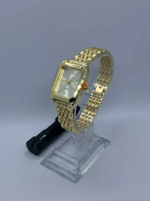 Guldfärgad damklocka med en band justerare - Bilderna visar en guldfärgad damklocka med rektangulär urtavla och gjord i rostfritt stål och ett nytt batteri