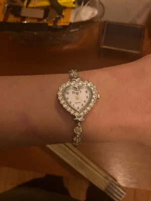 Silverfärgad klocka med hjärtformad urtavla - KÖP 2 FÅ EN TILL PRESENT 🎁   Söt damklocka med hjärtformad urtavla omgiven av strass. Armbandet är även det dekorerat med strass. Klockan har quartz urverk.  Skickar inom 24 timmar  Nytt batteri  Kvalitets kontroll  Säker parkering   Klockhållaren kommer inte med i köpet!