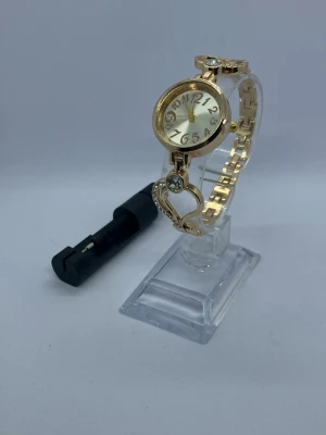 damklocka med guldfärgad boett och armband - KÖP 2 FÅ 1 PRESENT 🎁  Nytt batteri 🔋   Söt damklocka med guldfärgad boett och armband. Armbandet har hjärtformade detaljer med strass. Urtavlan är ljus med tydliga siffror.  Skickar inom 24 timmar Kvalitets kontroll Säker parkering  Klockhållaren kommer inte med i köpet!