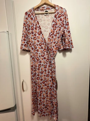 mönstrad wrap-klänning - ljusblå omlottklänning med röd-orangea blommor i stretchigt material från miss clarity! uppskattad storlek ca XL-XXL, skriv för mått m.m. <3