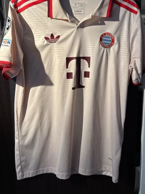 Bayern München Musiala tröja Adidas M - Säljer en beige Bayern München matchtröja från Adidas med Musiala och nummer 42 på ryggen. Tröjan har röda detaljer, klassisk krage och klubbmärke på bröstet. Tillverkad i polyester med slim fit passform och snygga röda ränder på axlar och ärmslut. Priset diskuteras