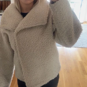 Beige teddyjacka med bred krage - Supermjuk och fluffig teddyjacka från Gina trickot i beige färg. Jackan har bred krage, lång ärm och en oversized passform som ger en chill vibe. Perfekt för kalla dagar när du vill vara både varm och snygg.