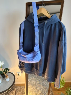 Ljuslila axelväska med justerbart band - Säljer en ljuslila axelväska med justerbart band och dragkedja. Väskan har en mjuk, puffig form och är tillverkad i syntetmaterial. Perfekt storlek för att bära det viktigaste och ger en cool vibe till din outfit.