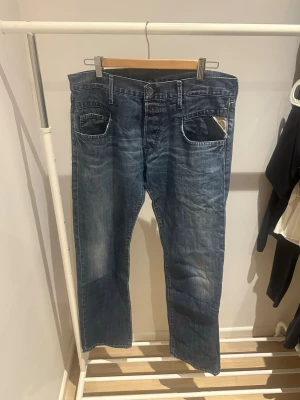 Replay jeans  - Säljer ett par klassiska blå jeans från Replay med raka ben och normal passform. Jeansen har fem fickor, snygga slitningar och Replay-logga på myntfickan. Materialet är robust denim i bomull och färgen är mörkblå med ljusare tvättade partier. Storleken är W32 och L34. Hör av er vid frågor eller funderingar 