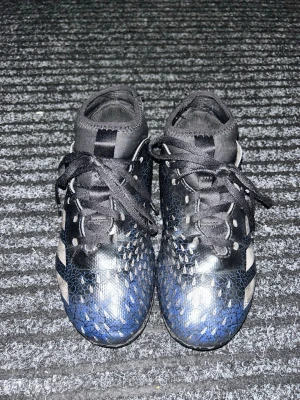 Adidas Predator fotbollsskor  - Adidas Predator fotbollsskor i svart och blått, med vita detaljer och med dobbar. Skorna är använda men funkar och är i storlek 35.