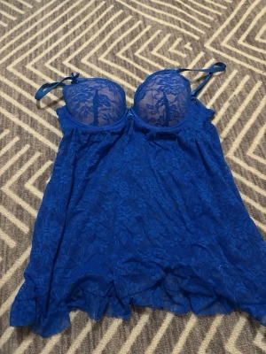 Blå spetlinne med volangdetaljer - Snyggt blå linne i transparent spets med blommigt mönster och volangkant. Axelbanden är smala och justerbara, och kuporna är push up för extra form. Kuporna är cirka C, men kan nog passa B också. 