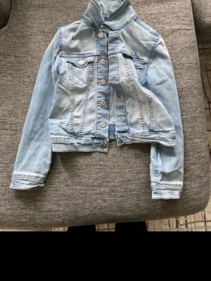 Ljusblå jeansjacka från &Denim - Säljer en ljusblå jeansjacka från &Denim med klassisk krage, långa ärmar och snygga knappar framtill. Jackan har två bröstfickor med lock och är tillverkad i slitstarkt jeanstyg. Perfekt för dig som gillar en chill och tidlös stil.