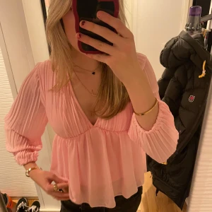 Rosa blus med v-ringning - Säljer en söt rosa blus med v-ringning och långa ärmar. Blusen har en luftig passform och är perfekt för både vardag och fest. Den är gjord i ett lätt och bekvämt material som faller fint.