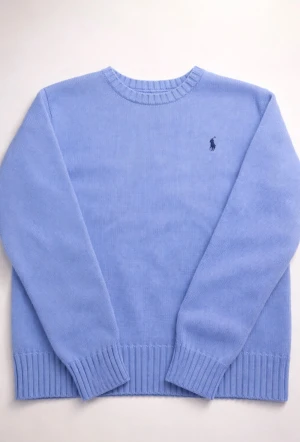 Ljusblå stickad tröja från Polo Ralph Lauren - Snygg ljusblå stickad tröja från Polo Ralph Lauren med klassisk rund hals och ribbade muddar. Tröjan har lång ärm och en liten broderad logga på bröstet. Perfekt för dig som gillar stilrena och tidlösa plagg. Liten i storlek passar m också 