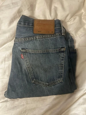 Levi's 501 blå jeans straight fit - Klassiska Levi's 501 jeans i blå tvätt med straight fit och normal passform. Jeansen har fem fickor, knappgylf och det ikoniska läderpatchen bak i midjan. Tillverkade i slitstarkt bomullsjeansmaterial. Perfekt för dig som gillar tidlös denimstil.