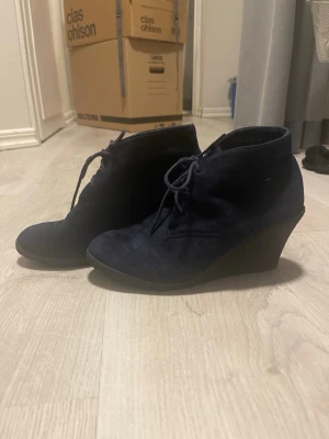 Mörkblå mocka stövletter med klack - Säljer ett par snygga mörkblå stövletter i mocka med snörning framtill och rund tå. Skorna har en stabil kilklack som ger extra höjd och stil. Perfekta för dig som vill ha en cool och dressad look. Passar till både jeans och kjol. Ny pris 300