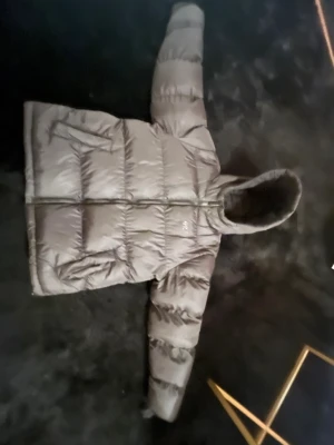 Svart pufferjacka från Hoodrich - Svart pufferjacka från Hoodrich med stor reflekterande logga på ryggen. Jackan har huva, dragkedja framtill och två sidofickor. Den är quiltad och har en loose passform som ger en chill vibe. Perfekt för kalla dagar när du vill se fresh ut.