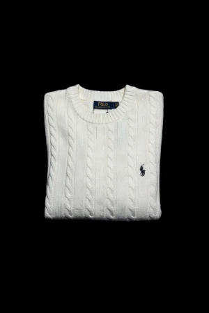 Vit kabelstickad väst från Polo Ralph Lauren - Vit kabelstickad väst från Polo Ralph Lauren med klassisk rund hals och broderad marinblå logga på bröstet. Västen har ribbade kanter och är gjord i mjukt bomullsmaterial. Perfekt för dig som gillar stilrena och tidlösa plagg.