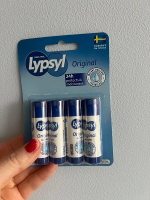 Lypsyl Original läppbalsam 4-pack - Fyra stycken Lypsyl Original läppbalsam i klassiska blå och vita hylsor. Innehåller bivax och kokosolja som återfuktar och skyddar läpparna med Instant Moisture Technology. Perfekt att ha med sig i väskan eller fickan för mjuka läppar hela dagen.