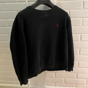 Svart sweatshirt från Polo Ralph Lauren - Svart sweatshirt från Polo Ralph Lauren med klassisk rund hals och röd broderad logga på bröstet. Tröjan har långa ärmar och ribbade muddar vid ärmslut och nederkant. Tillverkad i mjuk bomull för en skön och avslappnad stil. Tröjan är lite solblekt runt halsen därav priset. Bara att skriva om du har frågor!! Priset kan såklart diskuteras