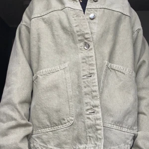 Olivgrön jeansjacka från Zara - Säljer en olivgrön jeansjacka från Zara med klassisk krage, stora bröstfickor och silverfärgade tryckknappar. Jackan är i jeans och har en avslappnad passform, perfekt att slänga över en hoodie eller t-shirt. Enkel och stilren design som funkar till det mesta.