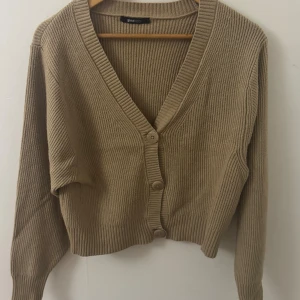  ribbad kofta från Gina Tricot - Säljer en beige brun ribbstickad kofta från Gina Tricot i storlek L. Koftan har v-ringning, långa ärmar och knäpps med tre knappar framtill. Perfekt att slänga över en topp för en chill look. Den är liten i passformen så funkar för en S 