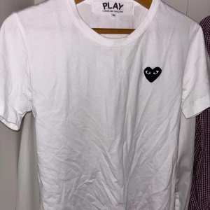 Vit Comme des Garçons Play t-shirt S - Vit t-shirt från Comme des Garçons Play i storlek S. Klassisk modell i bomull med korta ärmar och rund hals. På bröstet finns det ikoniska svarta hjärtat med ögon. Enkel och stilren design som passar till allt. Helt ny, köptes för ca 1 vecka sen. Säljer pga att den var lite för lite för mig. Jag är ca 180cm lång, passar de som är mellan 170-175.
