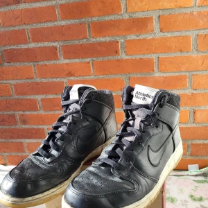 Nike Dunk High Svart Storlek 44 - Snygga Nike Dunk High sneakers i svart färg. Perfekt för vardagsbruk eller för att komplettera din outfit. Klassisk modell från Nike.