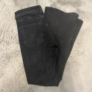 Svarta bootcut/flare jeans i storlek 38 - Snygga svarta jeans med klassisk femficksdesign och utsvängda ben. Jeansen har normalhög midja och är tillverkade i ett mjukt denimtyg som sitter skönt hela dagen. Perfekta för dig som gillar en enkel och stilren look. De är använda endast två gånger. Som nya. 