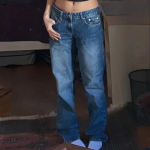 Blå raka jeans från Nelly - Säljer ett par klassiska blå jeans från Nelly med rak passform och normal midja. Jeansen har fem fickor, dragkedja och knapp framtill samt snygga slitningar för en avslappnad look. Perfekta till sneakers eller boots.