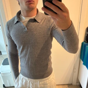 Grå pikétröja i ull från Peckham Rye - Snygg grå pikétröja från Peckham Rye i mjuk ull. Tröjan har klassisk krage, knäppning med två knappar och långa ärmar. Perfekt för dig som gillar stilrena och tidlösa plagg med en clean look. Bra skick men nopprig, sitter som XS