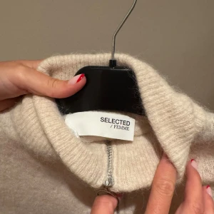 Beige kofta från Selected Femme - Mysig beige kofta från Selected Femme med hög krage och hel dragkedja framtill. Tröjan är stickad och har två fickor framtill. Har blivit krympt i tvätt och passar därför inte enligt storlek på lappen. Passar en XS. Har använts 5 gånger. 