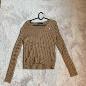 Beige kabelstickad tröja Polo Ralph Lauren - Kabelstickad beige tröja från Polo Ralph Lauren med v-ringning och broderad logga på bröstet.  I ett väldigt väldigt fint skick, oerhört sparsamt använd !🙏🏼🩷
