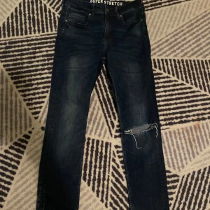 Mörkblå skinny jeans från &Denim - Mörkblå skinny jeans från &Denim med superstretch och slitning vid ena knät. Stretchigt denimtyg, perfekt för dig som gillar en tajt passform och lite ruffig look! 