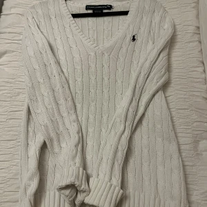 Vit kabelstickad tröja Ralph Lauren - Kabelstickad vit tröja från Ralph Lauren med v-ringning och klassisk broderad logga på bröstet. Tillverkad i 100% bomull och har långa ärmar samt ribbade muddar. Perfekt för lager-på-lager och snygg till jeans eller kjol. Buda gärna!