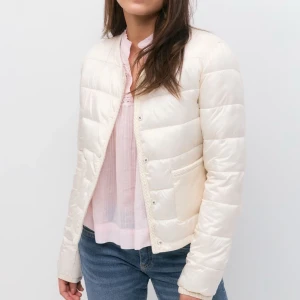 Ljusbeige pufferjacka från Gina Tricot - Supersnygg ljusbeige/vit pufferjacka från Gina Tricot med rund halsringning, två fickor framtill och knäppning med tryckknappar. Nypris 400kr.