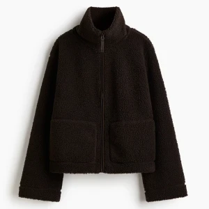 Mörkbrun teddyjacka med dragkedja - Aldrig använd, prislappen kvar. Mysig mörkbrun teddyjacka med hög krage och hel dragkedja framtill. Jackan har två stora fickor och är tillverkad i fluffigt teddy-material som håller dig varm och bekväm. Perfekt för kyliga dagar och enkel att styla till olika outfits. 